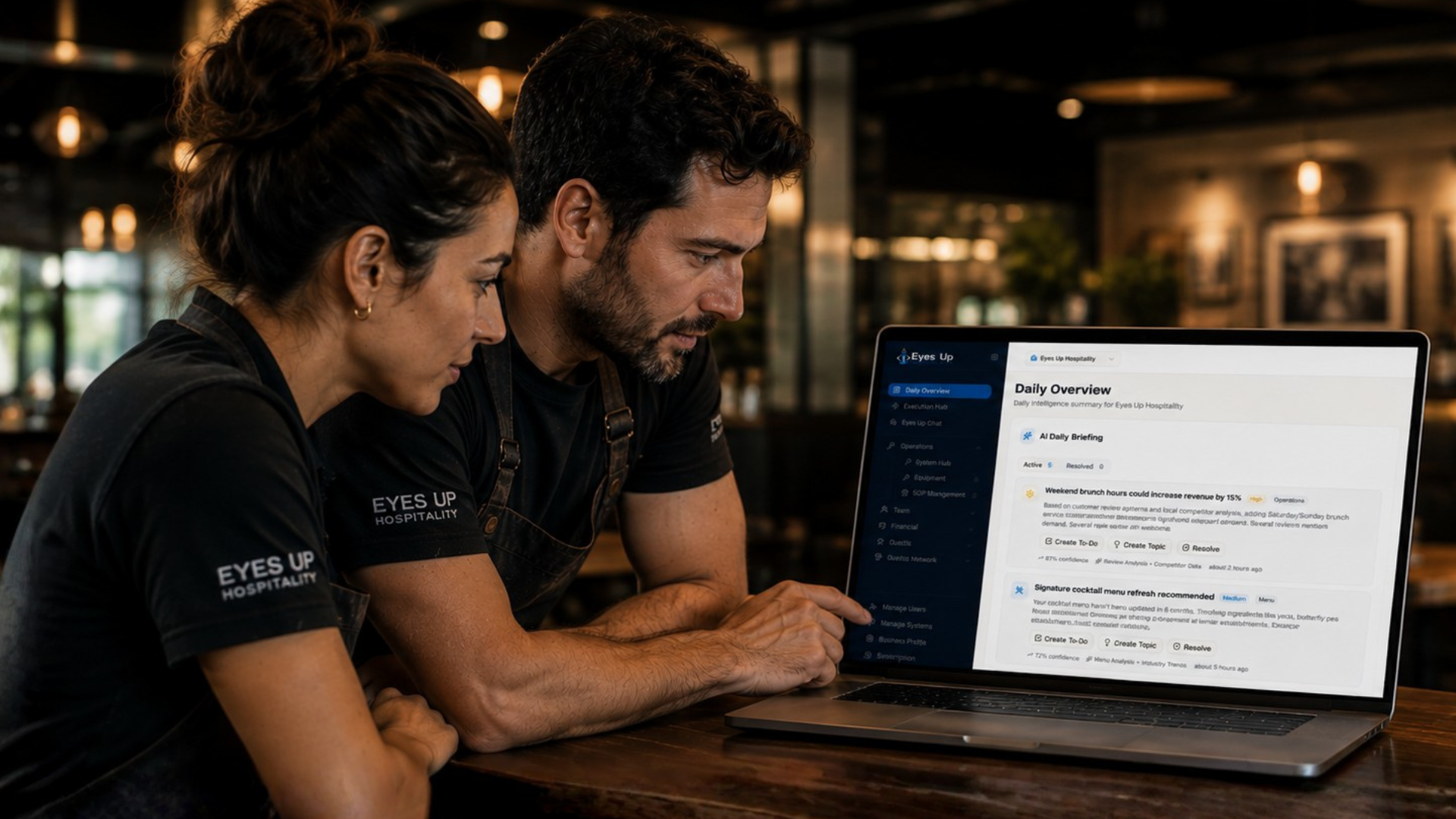 Two restaurant operators in Eyes Up Hospitality shirts reviewing the Daily Overview dashboard on a laptop